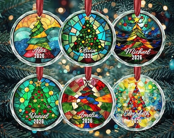 May include: Six circular glass ornaments featuring stained-glass style Christmas tree designs. Each ornament displays a unique tree pattern with vibrant colors, a red ribbon hanger, and personalized text including a name and the year 2026.