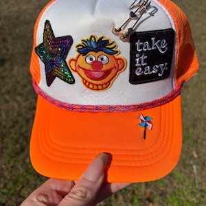 Il cappello più felice del mondo - Cappello da camionista arancione con toppa Ernie, stella di paillettes, scritta "Take It Easy" e dettagli con ciondolo / Unicorn Sober Studio