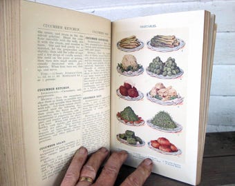 May include: An open vintage cookbook with a page showing a recipe for cucumber ketchup and a page showing a variety of vegetables, including asparagus, cauliflower, brussels sprouts, green beans, and potatoes.