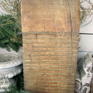 May include: A weathered, rectangular wooden washboard with a grooved lower section and a smooth upper section. The wood has a light brown color with visible grain and cracks, suggesting age and use. The washboard is a vintage laundry tool.