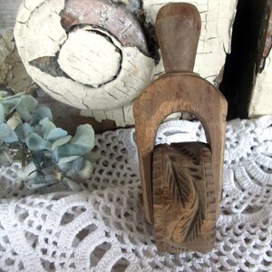 May include: A vintage wooden butter mold with a handle and a carved leaf design on the rolling cylinder. The mold is made of light brown wood and sits on a white lace doily.