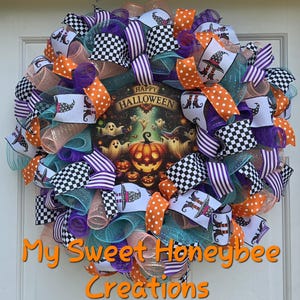 May include: A festive Halloween wreath with a central image of a glowing jack-o'-lantern, ghosts, and the words "Happy Halloween." The wreath features ribbons in orange, purple, black and white checkered, and teal, creating a colorful and spooky decoration.