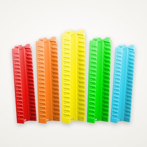 Pode incluir: Cinco suportes de armazenamento verticais em fila, cada um com uma cor distinta: vermelho, laranja, amarelo, verde e azul. Estes organizadores de plástico têm um canal central e painéis laterais com ranhuras horizontais espaçadas.