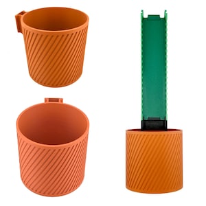 May include: Orange 3D-printed cup and holder set. The cup has a handle and diagonal ribbed texture. The holder has a green insert and a matching orange base with the same ribbed design. The set is designed for holding items.