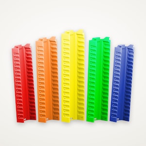 May include: Five vertical plastic rail covers arranged in a row, featuring a vibrant spectrum of colors including red, orange, yellow, green, and blue. Each piece has a textured, ridged surface with a central channel and notched edges.