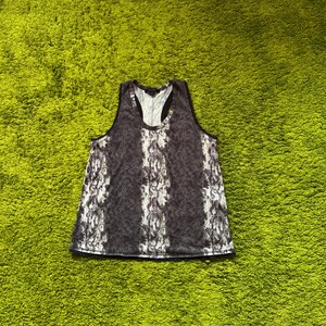 May include: A sleeveless tank top with a black and white snakeskin pattern. The top has a scoop neck and a black trim. The fabric appears to be lightweight and semi-sheer, with vertical stripes of the snakeskin design.