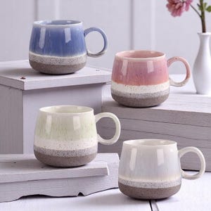May include: Four ceramic mugs with a speckled glaze in different colours: blue, pink, green, and grey. Each mug has a wide, rounded body and a handle.