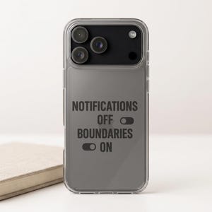 May include: A clear phone case with a gray backing featuring the text "NOTIFICATIONS OFF BOUNDARIES ON" in black. The phone case has a camera module with three lenses and is resting on a white surface.