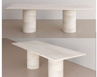 May include: A rectangular, light-colored stone table with two cylindrical supports. The table's surface has a subtle, natural grain pattern. The table is approximately 72 inches long and 36 inches wide.