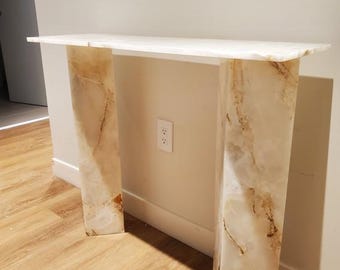 May include: White marble console table with two thick, rectangular legs. The table has a white top and a natural marble pattern on the legs.