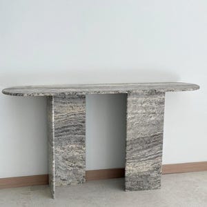 May include: A gray marble console table with an oval top and two rectangular legs. The table has a natural, veined pattern.
