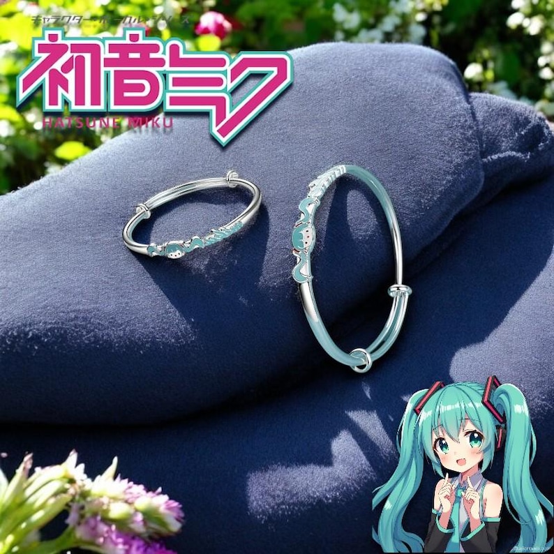 Pu&ograve; includere: Due braccialetti argentati con dettagli azzurri sono mostrati su una superficie blu scuro. I braccialetti presentano un design di personaggi dei cartoni animati. L'immagine include anche testo giapponese e un personaggio dei cartoni animati.
