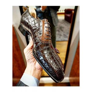 May include: Brown leather dress shoes with a crocodile pattern. The shoes have a lace-up closure and a pointed toe.