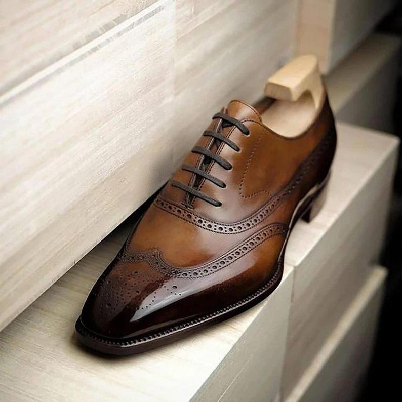 Puede incluir: Zapatos Oxford de cuero marr&oacute;n con dise&ntilde;o de punta de ala y cierre de cordones. Los zapatos tienen un acabado pulido y una punta puntiaguda.