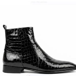 May include: A black ankle boot with a glossy, textured finish, resembling crocodile skin. The boot features a pointed toe, a low heel, and a pull tab at the back. The boot is set against a white background.