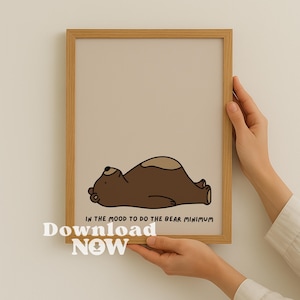 Puede incluir: Una impresión enmarcada con un oso de dibujos animados marrón, acostado sobre un fondo beige. El texto "IN THE MOOD TO DO THE BEAR MINIMUM" está debajo del oso. Las palabras "Download NOW" también son visibles.