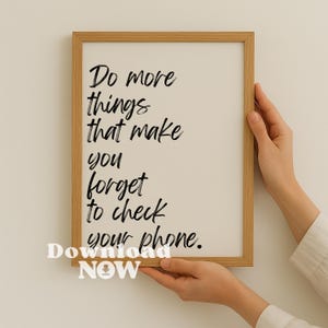 Könnte beinhalten: Gerahmter Druck mit dem Text "Tu mehr Dinge, die dich vergessen lassen, dein Handy zu checken." Der Druck befindet sich in einem Holzrahmen und wird von Händen gehalten. Die Wörter sind handschriftlich.