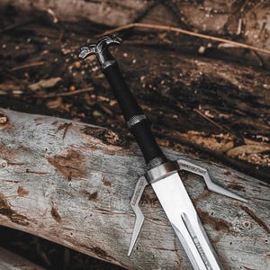May include: A silver and black sword with a detailed handle and a double-pronged guard, resting on a weathered wooden log. The sword's blade is polished, reflecting light, and the handle is wrapped in black material.