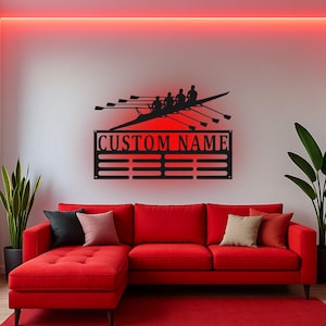 Puede incluir: Un letrero de pared de metal negro con la silueta de un equipo de remo de cuatro personas en un bote sobre un panel rectangular con el texto CUSTOM NAME y cuatro ranuras horizontales para colgar medallas, iluminado por una luz roja detrás.