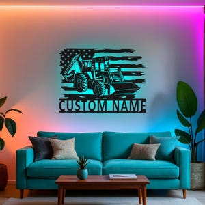 May include: Black metal wall art featuring a construction vehicle silhouette set against an American flag design. The text "CUSTOM NAME" is below the image. The artwork is mounted on a white wall above a teal sofa.