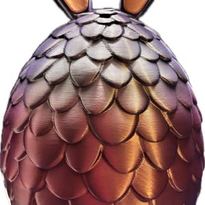May include: A decorative Easter egg sculpture with bunny ears. The egg is covered in overlapping, scale-like shapes that transition from purple to bronze. The bunny ears are bronze with a tan interior. The sculpture is a unique Easter decoration.