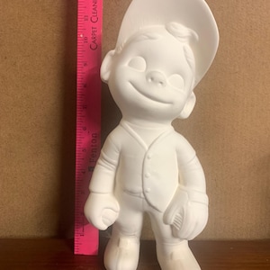 May include: A ceramic figurine of a smiling boy wearing a baseball cap, button-up shirt, and holding a baseball glove. The figurine is unpainted and ready for customization. The figure is approximately 10 inches tall.