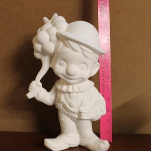 May include: White ceramic figurine of a clown holding a bunch of balloons. The clown is wearing a hat and a ruffled collar. The figurine is approximately 12 inches tall.