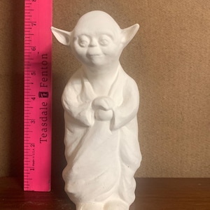 Puede incluir: Figura de cerámica blanca de un personaje de Star Wars, Yoda, de pie con las manos juntas frente a él. La figura mide aproximadamente 15 cm de alto.