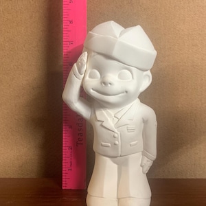 May include: White ceramic figurine of a person in a sailor uniform saluting. The figurine is approximately 18 cm tall.