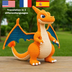 Op de afbeelding: Een gehaakt drakenknuffeltje met een feloranje lichaam, een crèmekleurige buik en onderkant van de staart. Het wezen heeft grote blauwe ogen, witte klauwen aan de handen en voeten, en donkerblauwe vleugels met een gestructureerd uiterlijk.