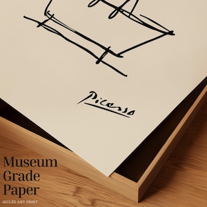 May include: A framed print featuring a black line drawing and the signature "Picasso." The words "Museum Grade Paper" are printed in a stacked format. The artwork is set in a wooden frame.
