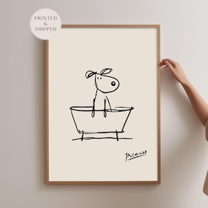 May include: A framed art print featuring a minimalist black line drawing of a dog in a bathtub. The artwork is signed "Picasso" and includes the text "Printed & Shipped" in a circular sticker.