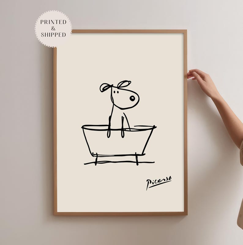 May include: A framed art print featuring a minimalist black line drawing of a dog in a bathtub. The artwork is signed "Picasso" and includes the text "Printed & Shipped" in a circular sticker.