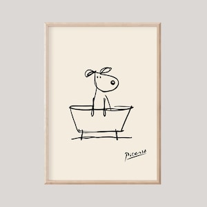 May include: A framed art print featuring a whimsical line drawing of a dog in a bathtub. The black ink illustration is set against a cream background, with the artist's signature in the lower right corner. The artwork has a minimalist style.