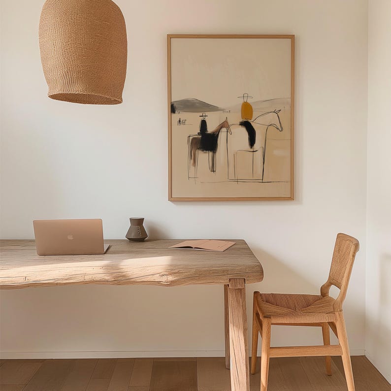 May include: An abstract art print in a wooden frame depicts riders on horses in a minimalist style. The artwork hangs above a wooden desk with a laptop, a small vase, and a notebook. A woven chair sits beside the desk, and a woven light fixture hangs above.