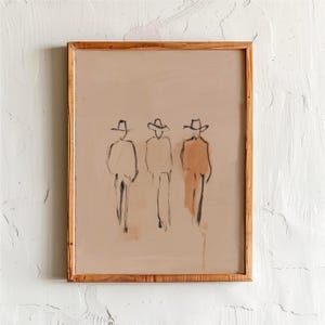 Puede incluir: Impresi&oacute;n art&iacute;stica abstracta que presenta tres figuras con sombreros de vaquero, esbozadas en negro sobre un fondo beige. La obra de arte est&aacute; enmarcada en un marco de madera natural. Las figuras se representan con l&iacute;neas simples y sombreado.
