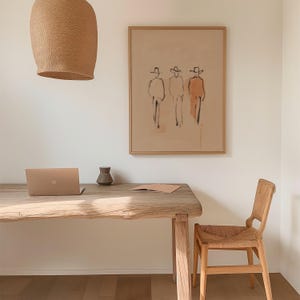 Puede incluir: Un espacio de oficina en casa de tonos neutros con un escritorio de madera, un port&aacute;til y una silla de mimbre. Una obra de arte enmarcada con figuras abstractas cuelga de la pared. Una l&aacute;mpara colgante tejida cuelga sobre el escritorio. Un peque&ntilde;o jarr&oacute;n y un cuaderno est&aacute;n sobre el escritorio.