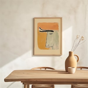 Op de afbeelding: Abstracte kunstprint in een houten lijst. Het kunstwerk toont een stierenkop met een oranje achtergrond en een zwarte lijntekening. Een beige vaas en een klein wit kopje staan op een houten tafel.