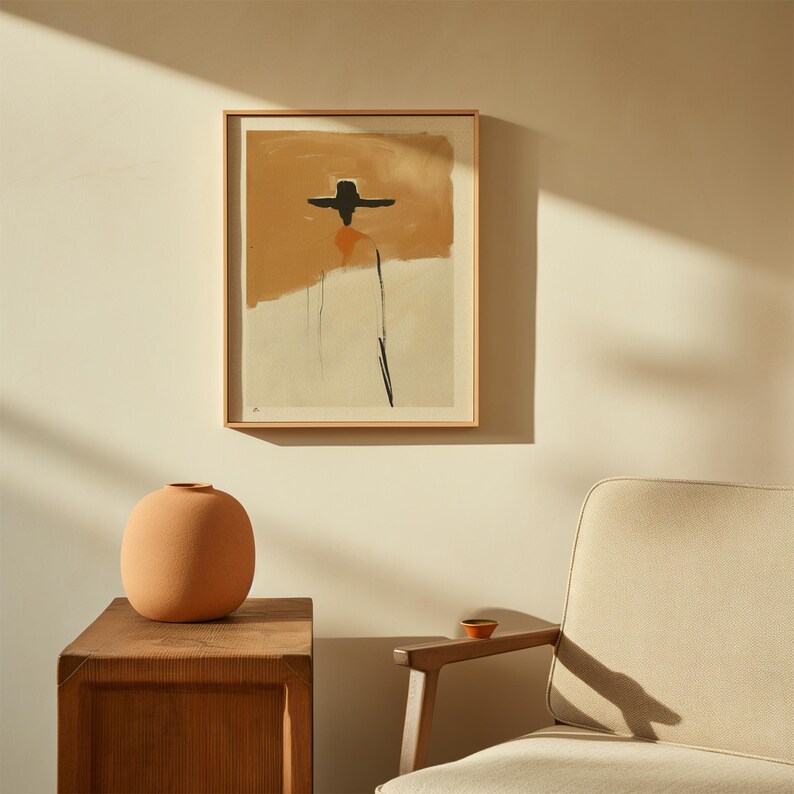 K&ouml;nnte beinhalten: Abstrakter Kunstdruck in einem Holzrahmen mit einem schwarzen Hut und einer Figur auf beigem und orangefarbenem Hintergrund. Eine Terrakotta-Vase steht auf einem h&ouml;lzernen Beistelltisch. Im Hintergrund ist ein beigefarbener Sessel zu sehen.