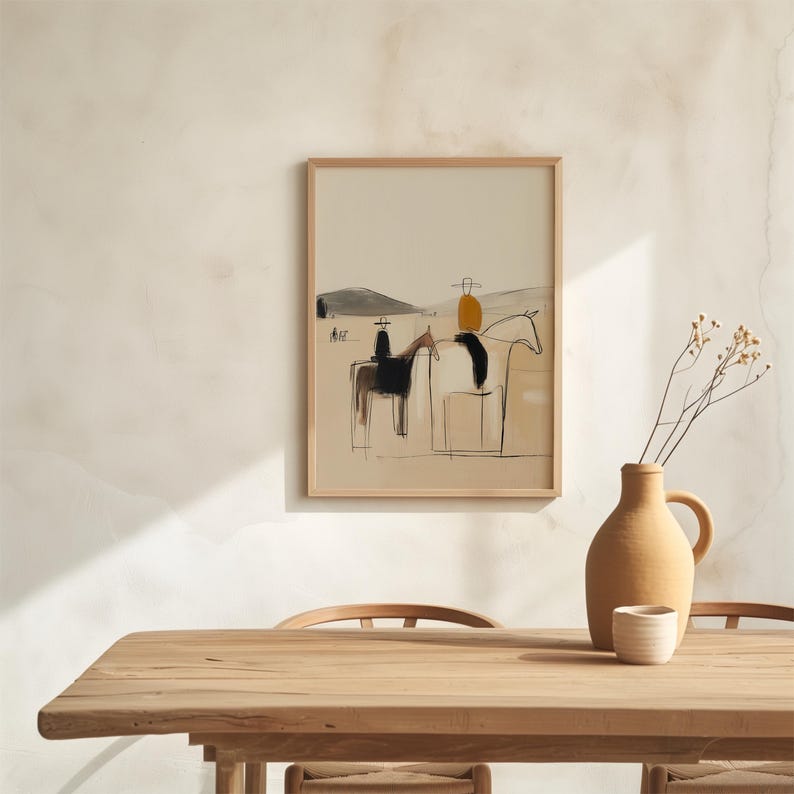 May include: Abstract art print in a light wood frame. The artwork depicts riders on horseback in a minimalist style, using black, brown, and yellow tones. A ceramic vase and small cup sit on a wooden table in the foreground.