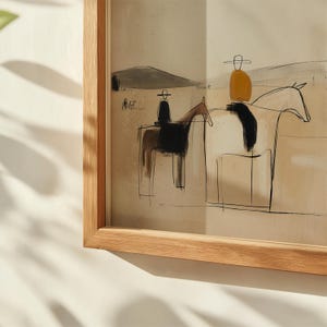 May include: Abstract art print featuring two riders on horseback, rendered in a minimalist style with black and brown ink. The riders wear hats and are set against a neutral background with a mountain silhouette. The artwork is framed in a natural wood frame.