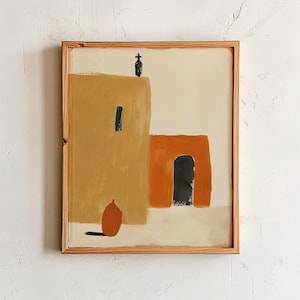 May include: A framed wall art print featuring a stylized illustration of two adobe-style buildings in shades of mustard yellow and burnt orange. The scene includes a dark doorway, a small black cross on the roof, and a terracotta-colored vessel.