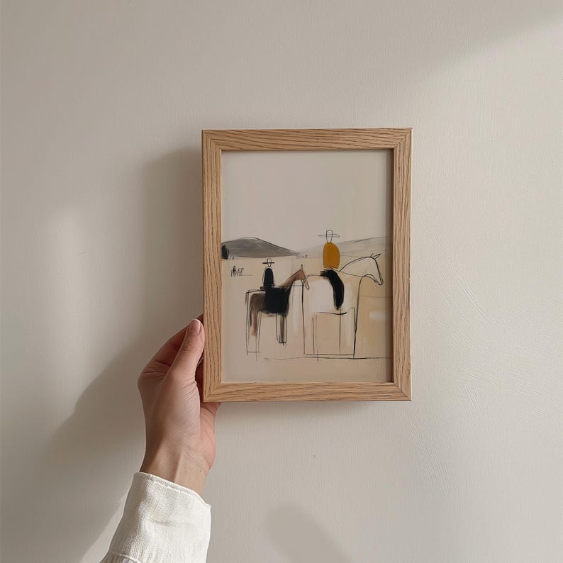 May include: A framed art print featuring a minimalist illustration of two horses with riders. The artwork uses a neutral color palette with black, tan, and yellow accents. The frame is made of light-colored wood.