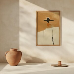 K&ouml;nnte beinhalten: Abstrakter Kunstdruck in einem Holzrahmen. Das Kunstwerk zeigt eine Figur mit schwarzem Hut und orangefarbenem und beigem Hintergrund. Eine Terrakotta-Vase und eine kleine Tasse stehen auf einem Holztablett.
