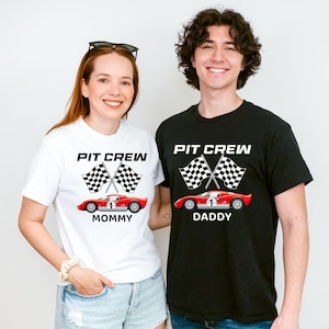 Op de afbeelding: Twee mensen dragen bijpassende t-shirts. Het witte shirt zegt "Pit Crew Mommy" en het zwarte shirt zegt "Pit Crew Daddy". Beide shirts hebben een rode raceauto en geblokte vlaggen.
