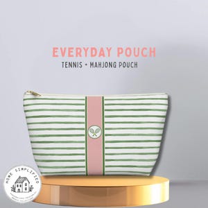 Könnte beinhalten: Eine weiß-grün gestreifte Tasche mit goldenem Reißverschluss. Ein rosa vertikaler Streifen mit einem Tennisschläger-Logo ist auf der Tasche zentriert. Der Text auf dem Bild lautet "EVERYDAY POUCH TENNIS + MAHJONG POUCH".