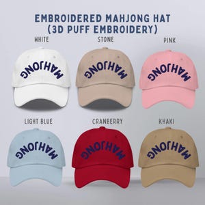 May include: Six baseball caps in white, stone, pink, light blue, cranberry, and khaki. Each cap features the text MAHJONG in dark blue 3D puff embroidery. The text EMBROIDERED MAHJONG HAT (3D PUFF EMBROIDERY) appears at the top of the image.