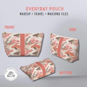 May include: A cosmetic pouch with a camouflage design in pink, peach, and brown. It features a peach stripe and a gold zip. The image text says "EVERYDAY POUCH" and "MAKEUP • TRAVEL • MAHJONG TILES". The pouch is designed for makeup, travel, and mahjong tiles.