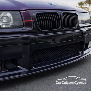 May include: A dark purple BMW car front end featuring a black kidney grille, a lower mesh air intake, and clear headlights. A thin red horizontal stripe accents the hood near the grille. The text CarCultureCyprus is visible in white.
