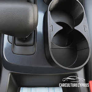 May include: A black car cup holder with two circular openings and a separate single cup holder. The cup holders are made of a textured material and are designed to fit into a car's centre console. The image also shows a gear shift and the Car Culture Cyprus logo.